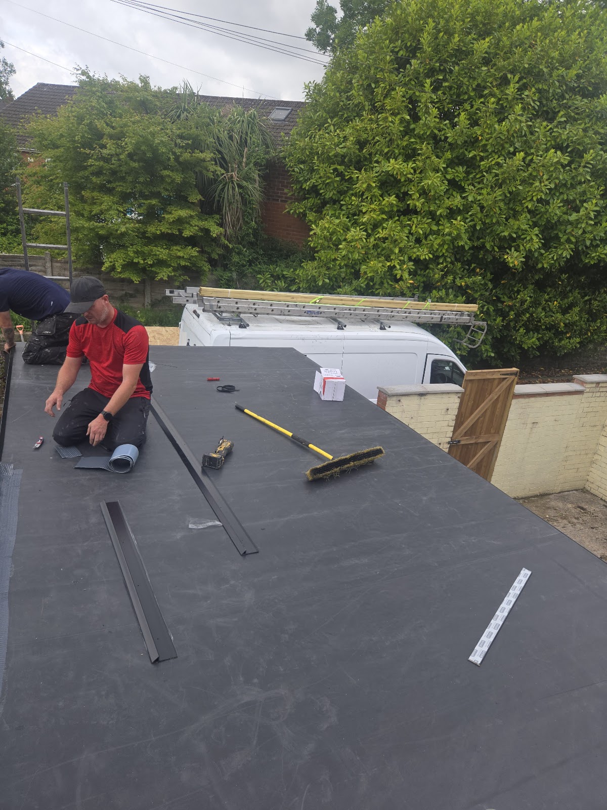 Two workers fitting flat roofing with tools and strips of roofing material